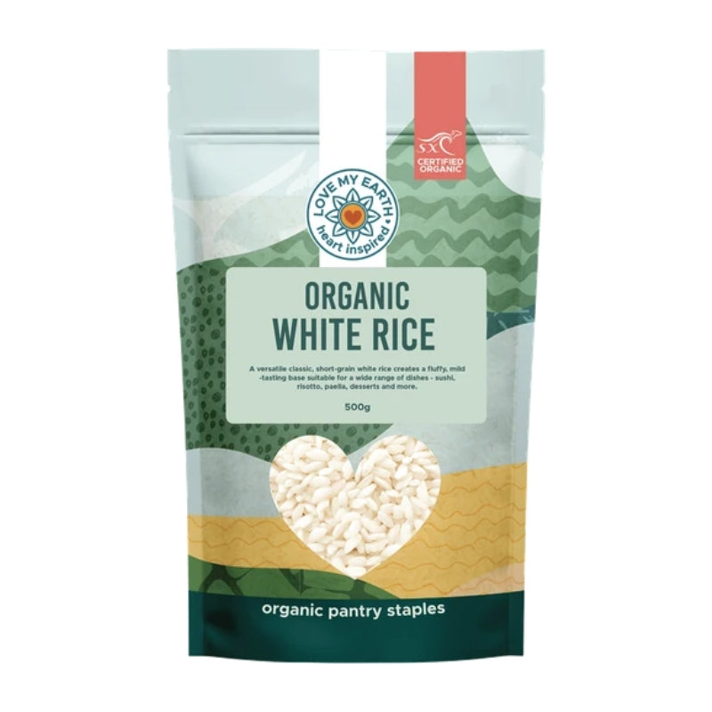 A 500g stand-up pouch of Love My Earth Organic White Rice on a plain white background. The packaging features a light blue top section, a green wavy pattern band, a beige textured band, and a heart-shaped clear window showing the white rice inside.