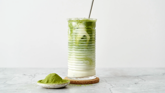 Layered matcha latte in a glass with matcha powder, made with organic ingredients