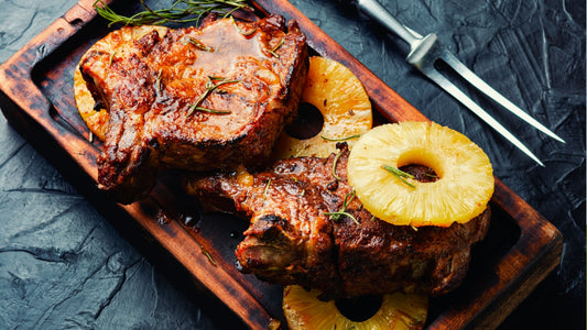 Grilled pork chops glazed with sauce and garnished with fresh rosemary, served with juicy pineapple rings on a rustic wooden board.