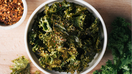 Crispy kale chips sprinkled with chili flakes in a white bowl.