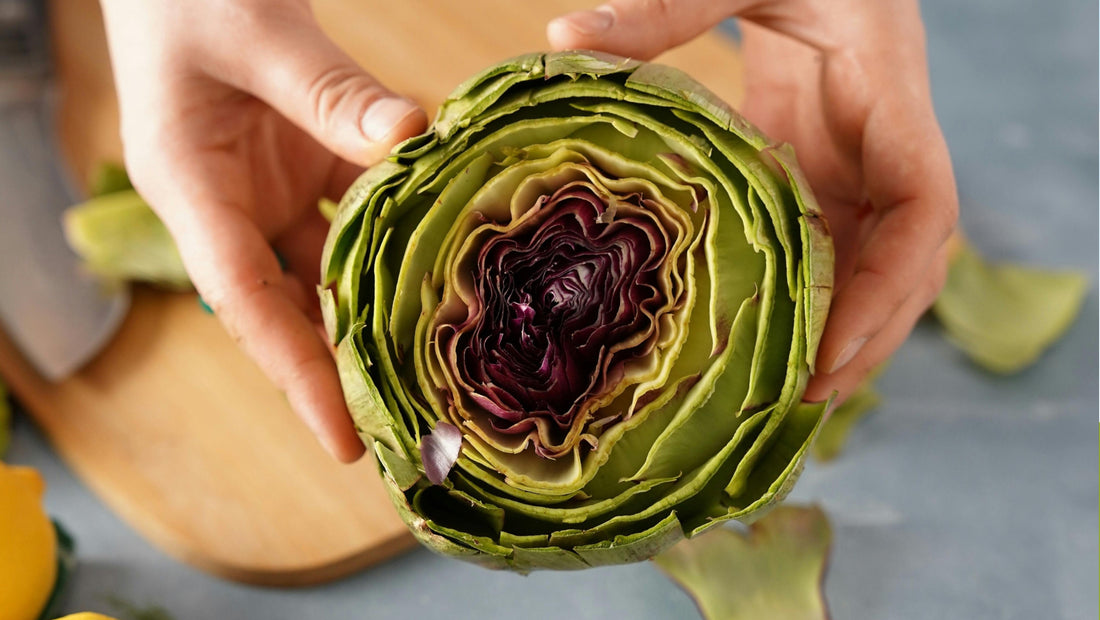 Close-up of a fresh globe artichoke cut in half, showing its layered green leaves and deep purple centre.