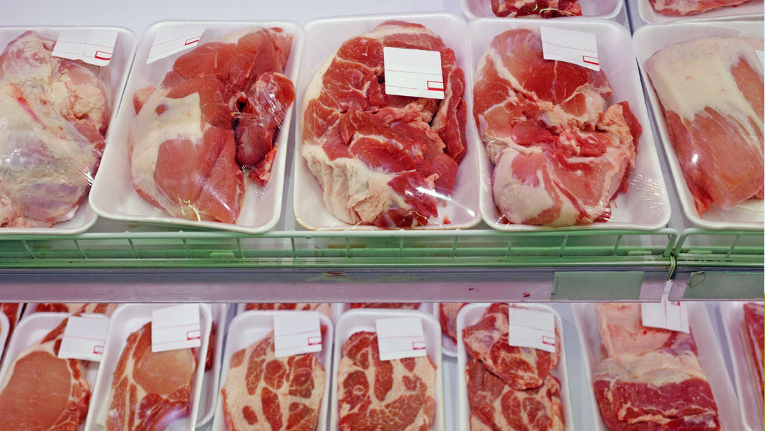 Packaged raw meat cuts wrapped in clear plastic on white trays in a refrigerated supermarket meat display.