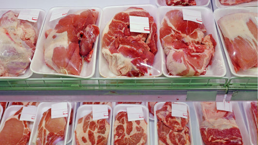 Packaged raw meat cuts wrapped in clear plastic on white trays in a refrigerated supermarket meat display.