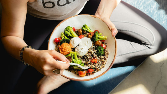 Person holding a colourful quinoa bowl with broccoli, cherry tomatoes, mushrooms and sliced cheese, illustrating simple healthy eating habits.