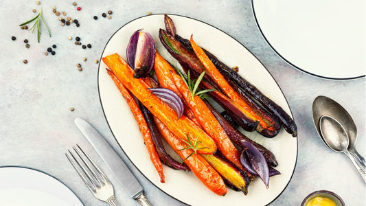 Raw honey glazed organic purple and orange carrots and red onion with rosemary sprigs on a white plate