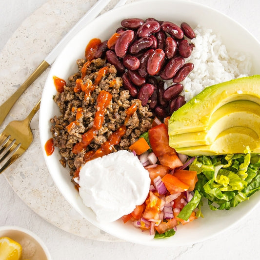 Plated dish with ground meat, beans, avocado, tomatoes, and lettuce on a white plate.