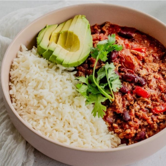 Bowl with rice, chili, avocado, and cilantro on a light background