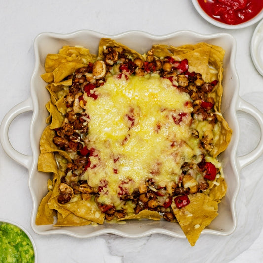Nacho dish with melted cheese and vegetables on a white plate.