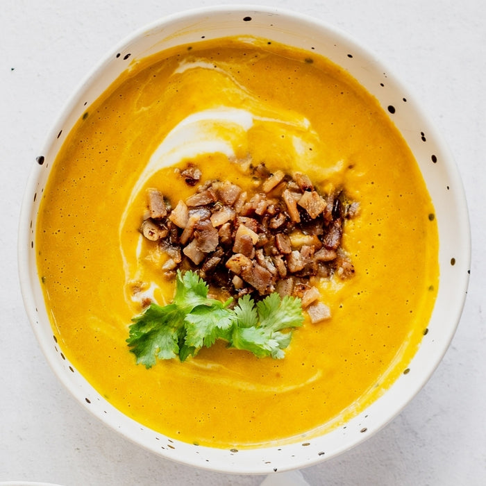 Pumpkin soup in a white bowl with garnishes on a light background
