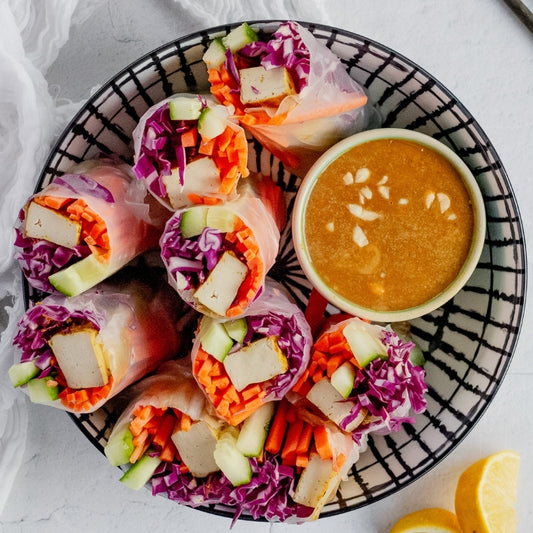 Colorful rice paper rolls with a dipping sauce on a decorative plate.