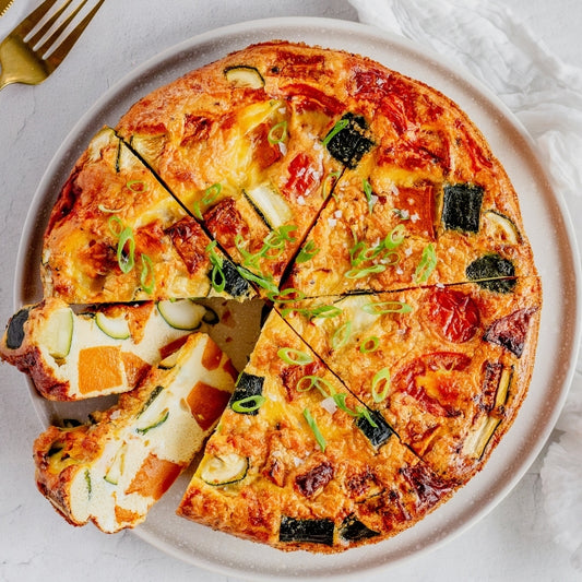 Vegetable frittata sliced on a plate with a fork on a marble surface