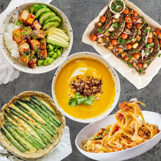 Assorted dishes including a bowl of soup, a plate of pasta, and other food items on a gray surface.