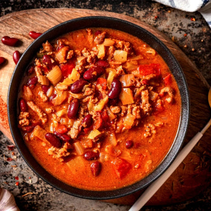  bowl of chili with ground beef, beans, and vegetables on a wooden board