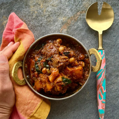 Bowl of moroccan lamb with a decorative spoon on a textured surface